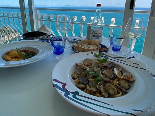 Terrace table with a view of the sea, set with clams and a pasta dish
