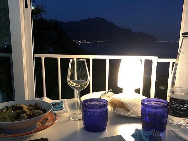 Evening table on the terrace, with a glass of white wine and the lights of the coast