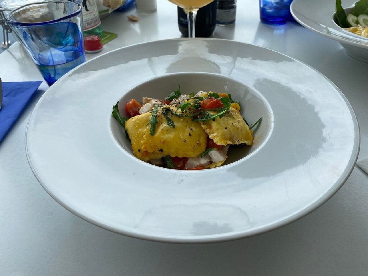 Ravioli with cherry tomatoes and herbs, served on a table set with blue glasses