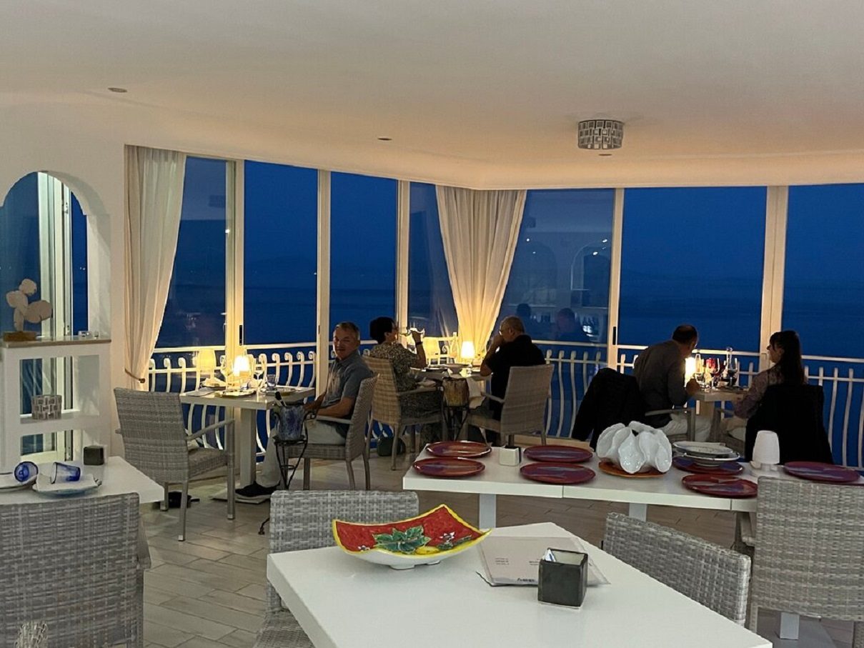 Dining room at night with candle-lit tables and large windows facing the sea